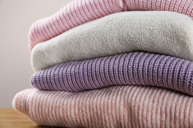 Photo of Stack of knitted sweaters on wooden table, closeup