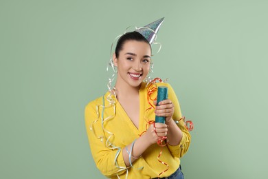 Young woman blowing up party popper on pale green background