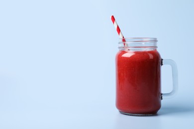 Photo of Mason jar with delicious berry smoothie on light blue background. Space for text