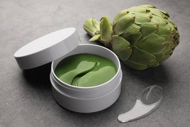 Photo of Package of under eye patches and artichoke on grey table, closeup. Cosmetic product