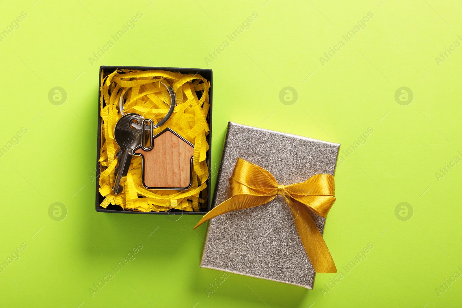 Photo of Key with trinket in shape of house and gift box on light green background, flat lay. Housewarming party