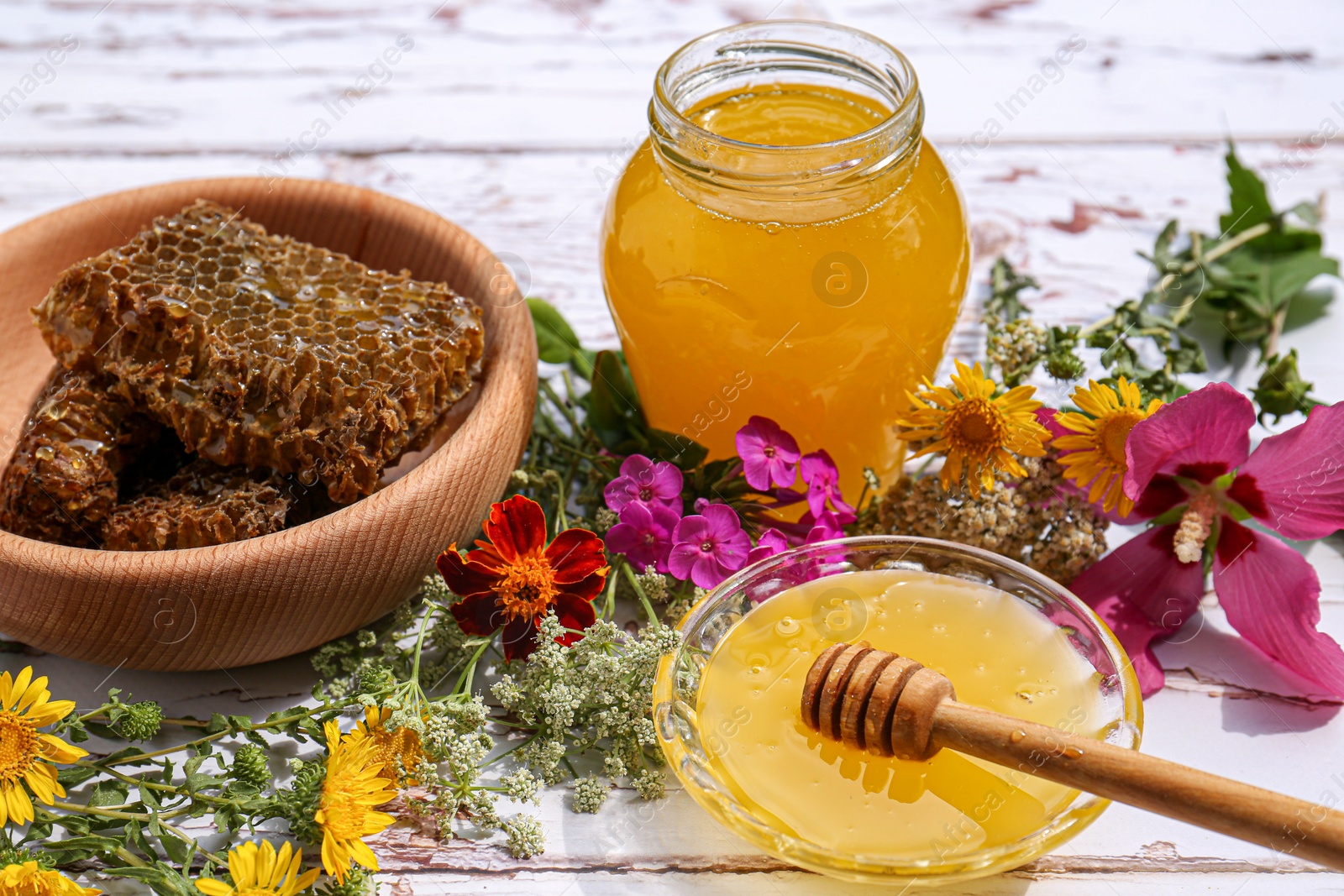 Photo of Delicious honey, combs and different flowers on white wooden table