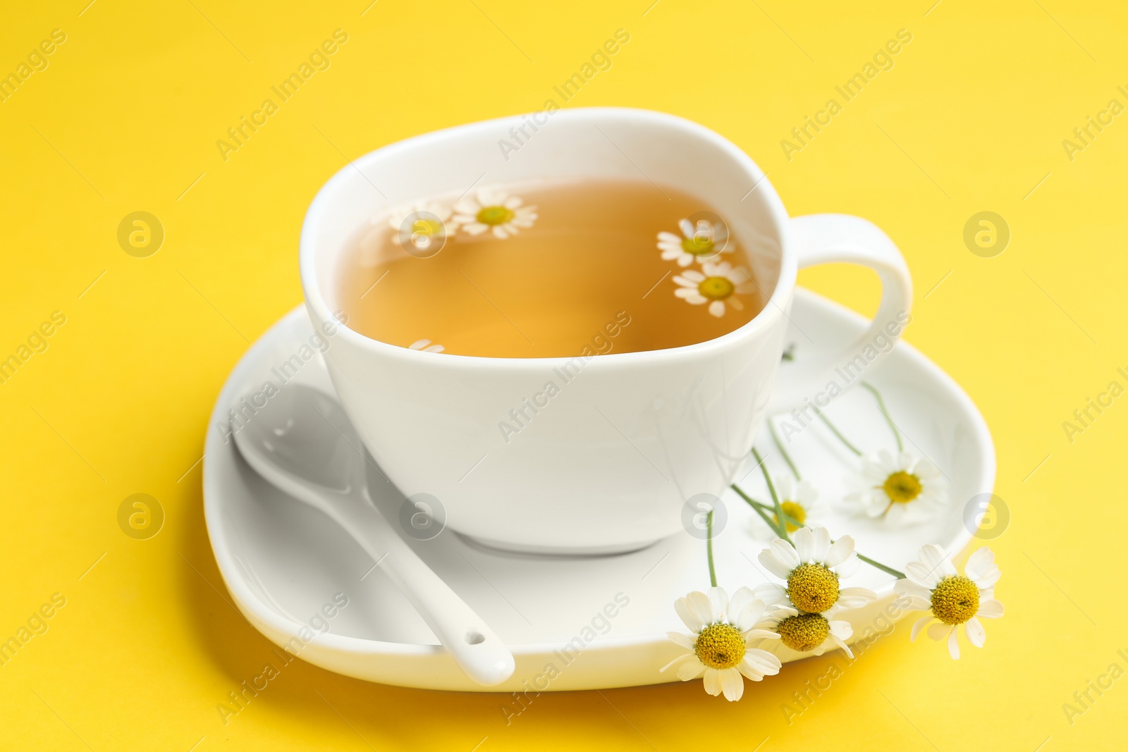 Photo of Delicious chamomile tea in cup on yellow background