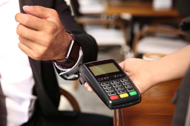 Photo of Man making payment with smart watch in cafe, closeup