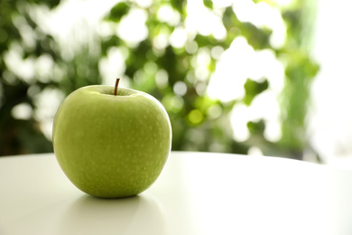 Fresh ripe green apple on white table against blurred background, closeup. Space for text