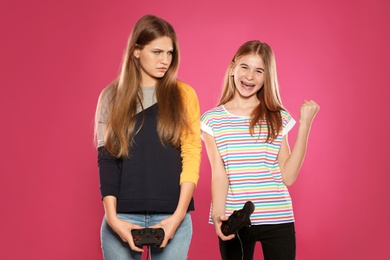 Photo of Young woman and teenage girl playing video games with controllers on color background