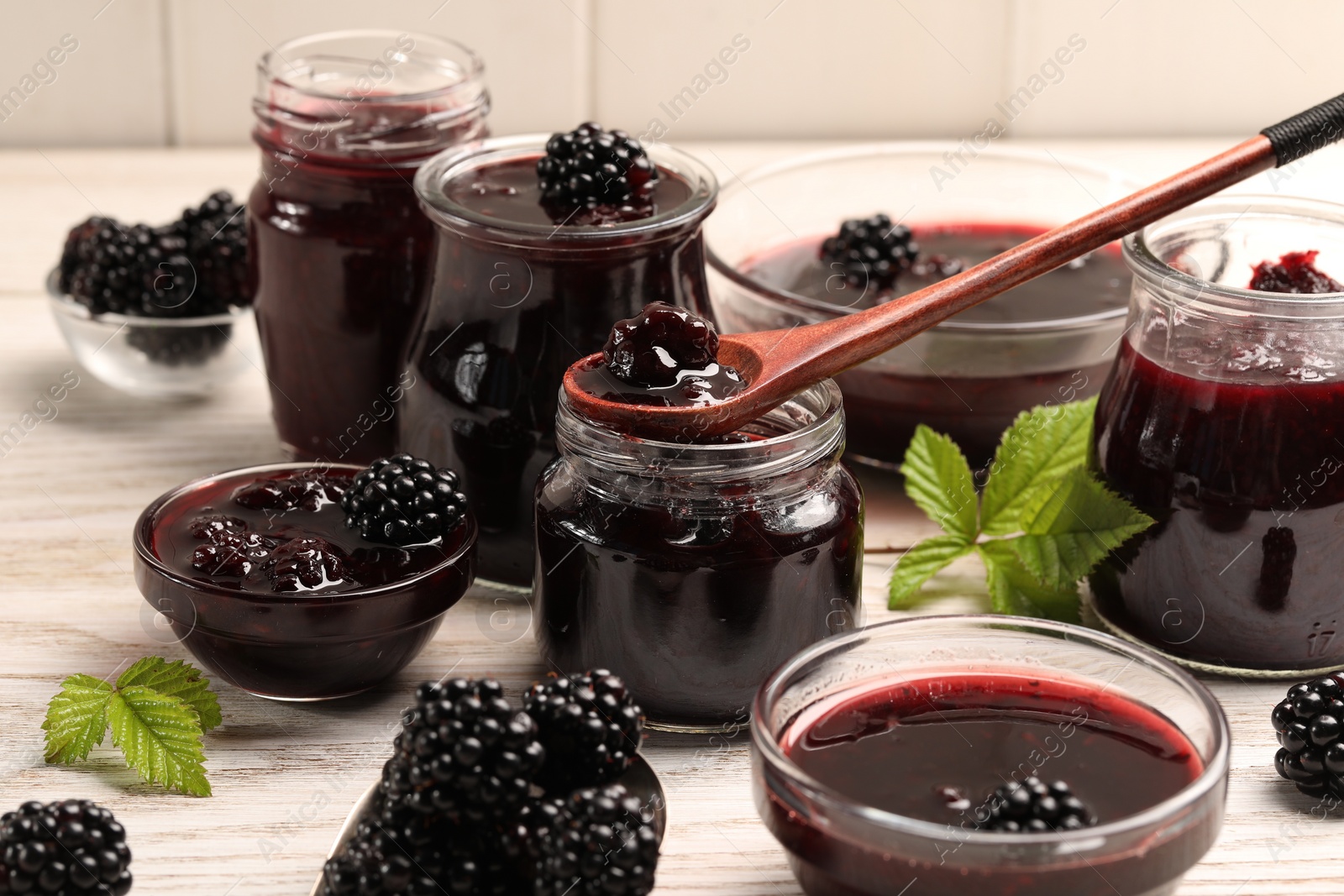 Photo of Taking tasty blackberry jam with spoon on white wooden table