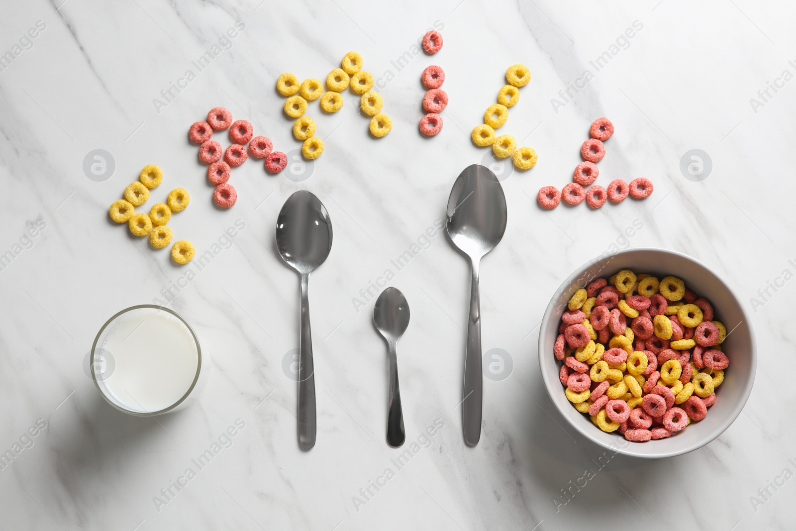 Photo of Word Family, cereal rings, milk and different spoons on white marble table, flat lay