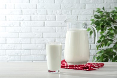 Jug and glass of fresh milk on white wooden table, space for text
