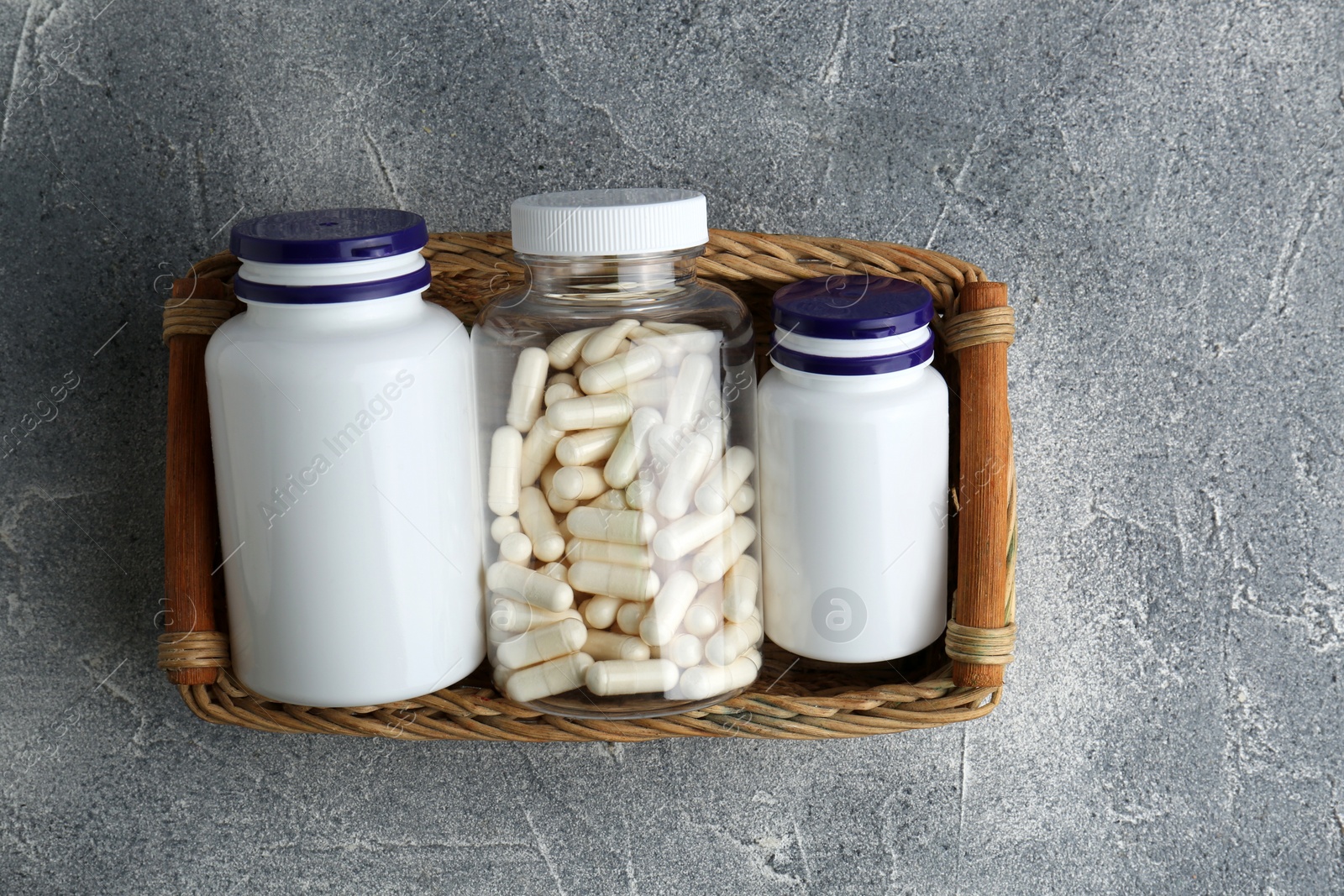 Photo of Medical bottles with pills in wicker tray on light gray textured table, top view