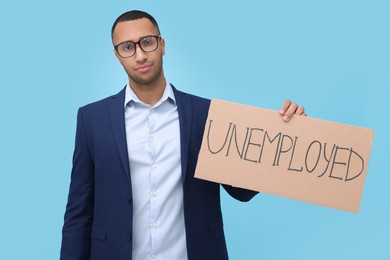 Young man holding sign with word Unemployed on light blue background