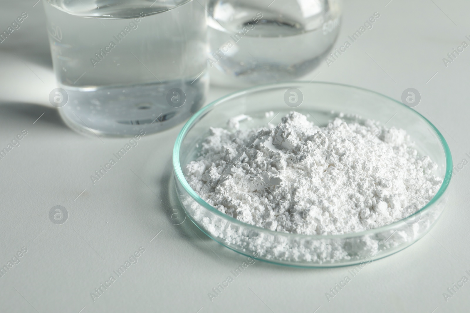 Photo of Petri dish with calcium carbonate powder and laboratory glassware on white table