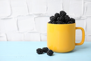 Fresh ripe blackberries in yellow mug on light blue wooden table. Space for text