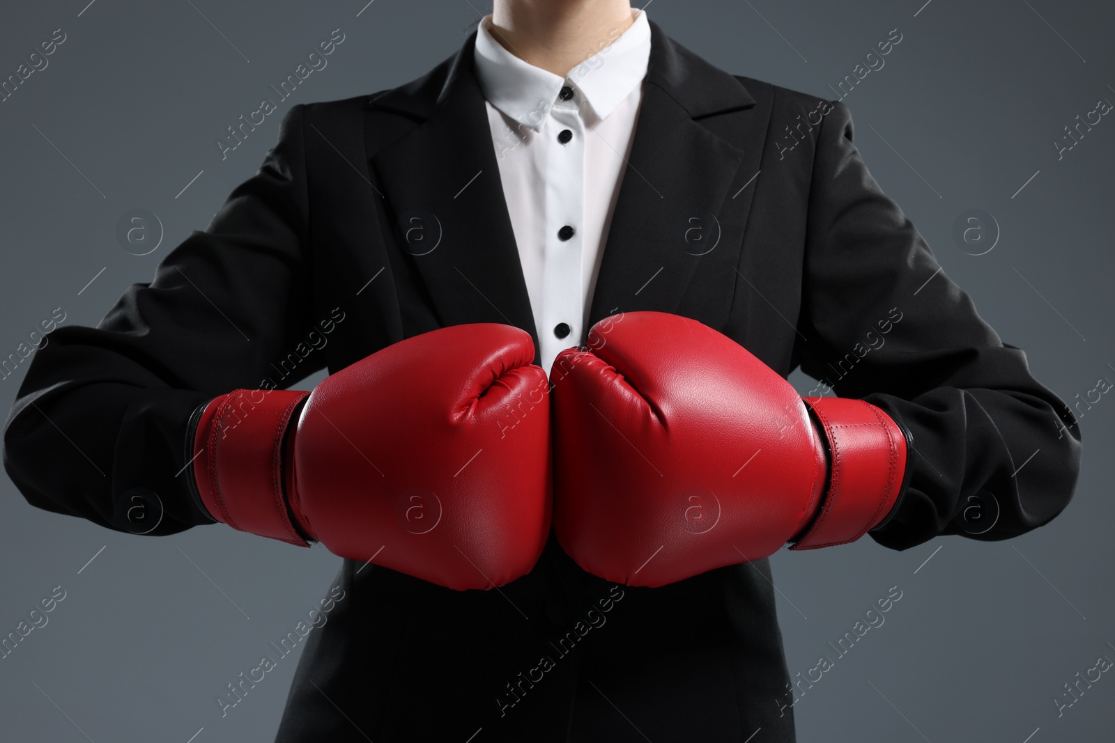 Photo of Businesswoman in suit wearing boxing gloves on grey background, closeup