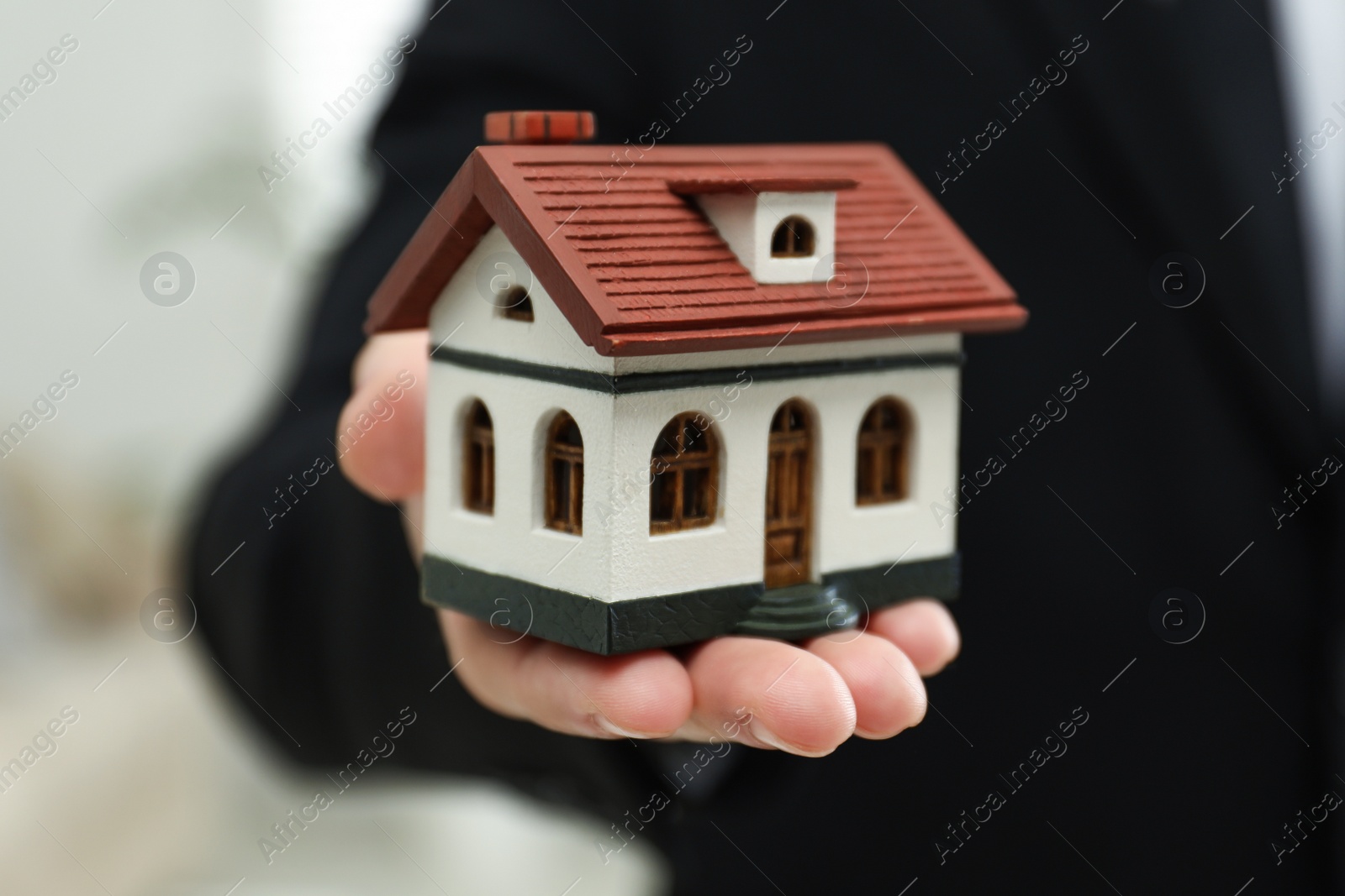 Photo of Real estate agent holding house model indoors, closeup