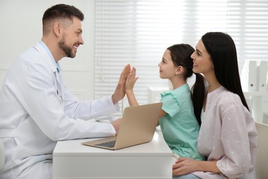 Mother with daughter visiting pediatrician in hospital. Doctor giving high five to little girl