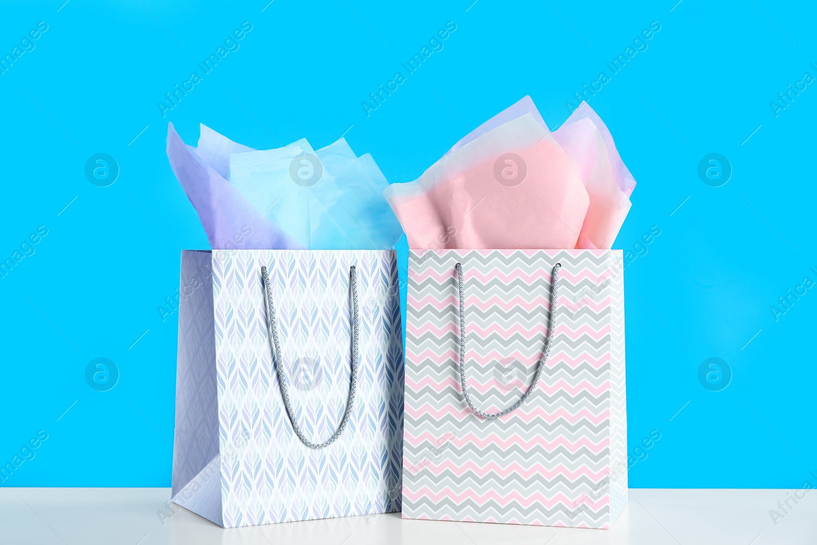 Photo of Gift bags with paper on white table against light blue background