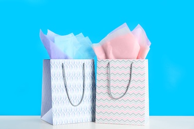 Photo of Gift bags with paper on white table against light blue background