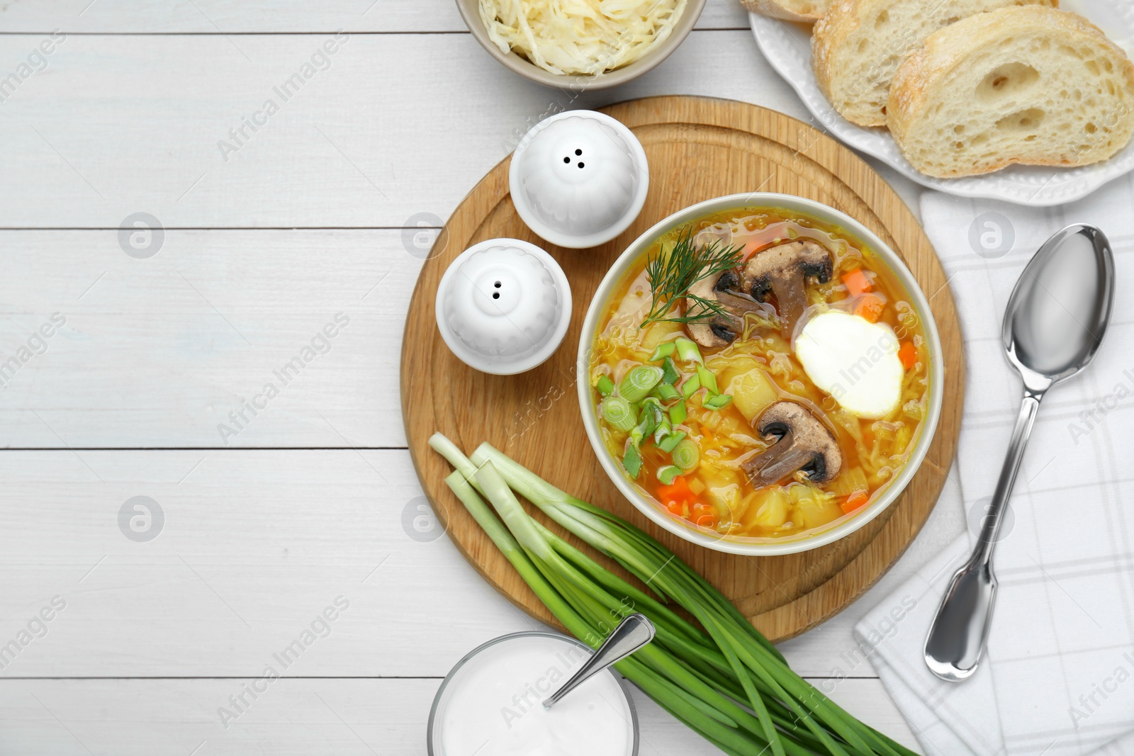 Photo of Delicious sauerkraut soup with mushrooms, green onion, dill and sour cream served on white table, flat lay. Space for text