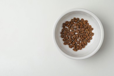 Feeding bowl with dry cat food on white background, top view. Space for text