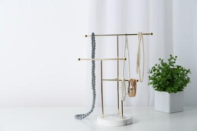 Interior element. Holder with set of luxurious jewelry and houseplant on white table. Space for text