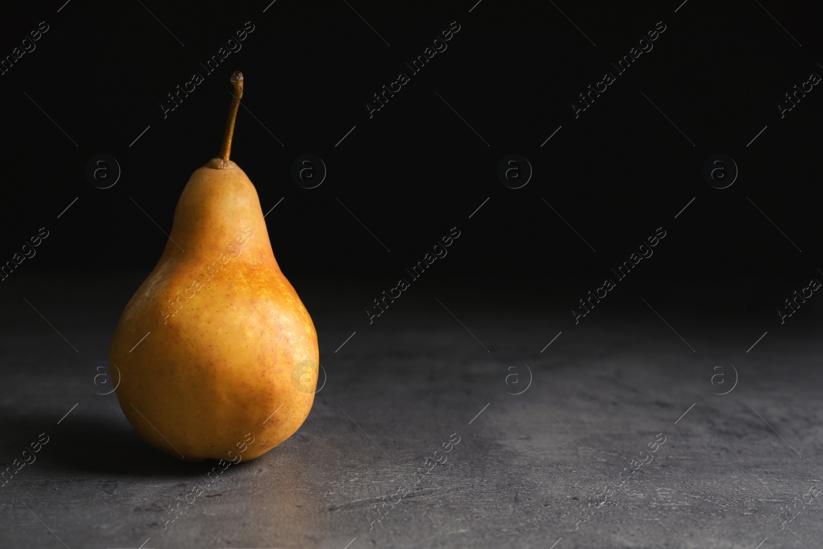 Photo of Ripe pear on table against black background. Space for text