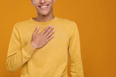 Photo of Thank you gesture. Grateful man with hand on chest against orange background, closeup