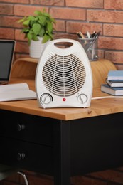 Photo of Modern electric fan heater near notebooks on wooden table in office