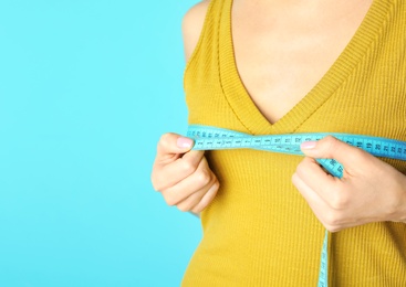 Photo of Young woman measuring breast size on color background, closeup view with space for text. Cosmetic surgery