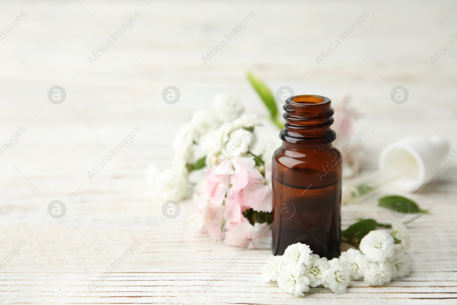 Photo of Bottle of essential oil and flowers on table