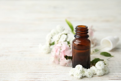 Bottle of essential oil and flowers on table