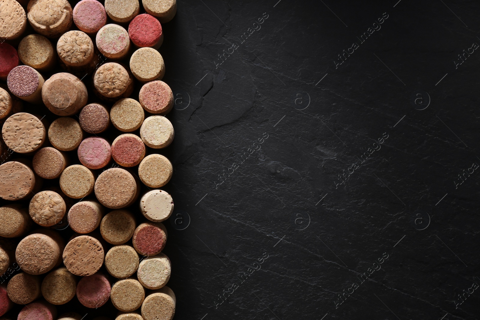 Photo of Many wine bottle corks on black table, flat lay. Space for text