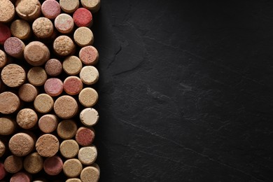 Photo of Many wine bottle corks on black table, flat lay. Space for text