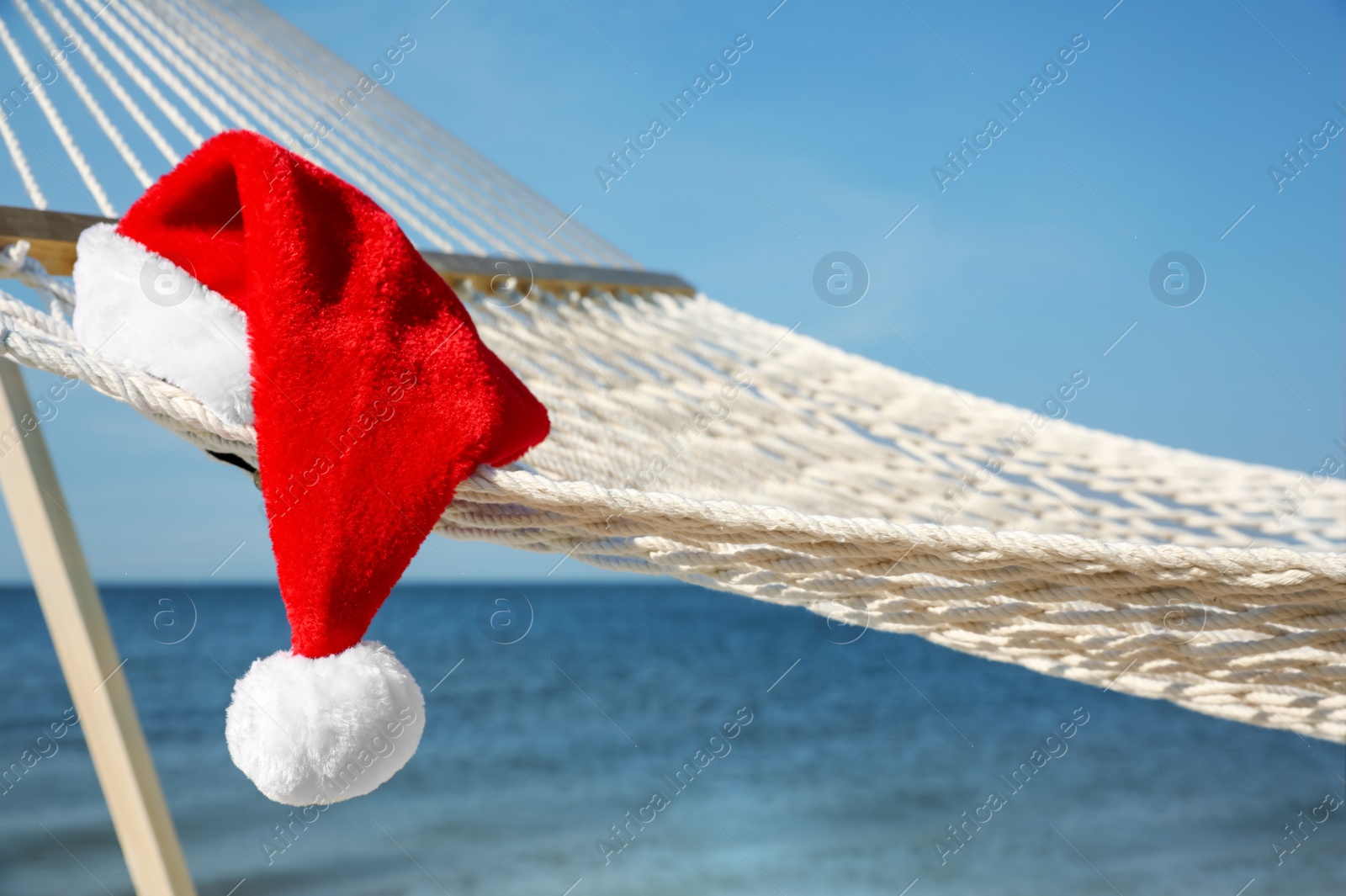 Photo of Rope hammock with Santa's hat on beach, closeup. Christmas vacation