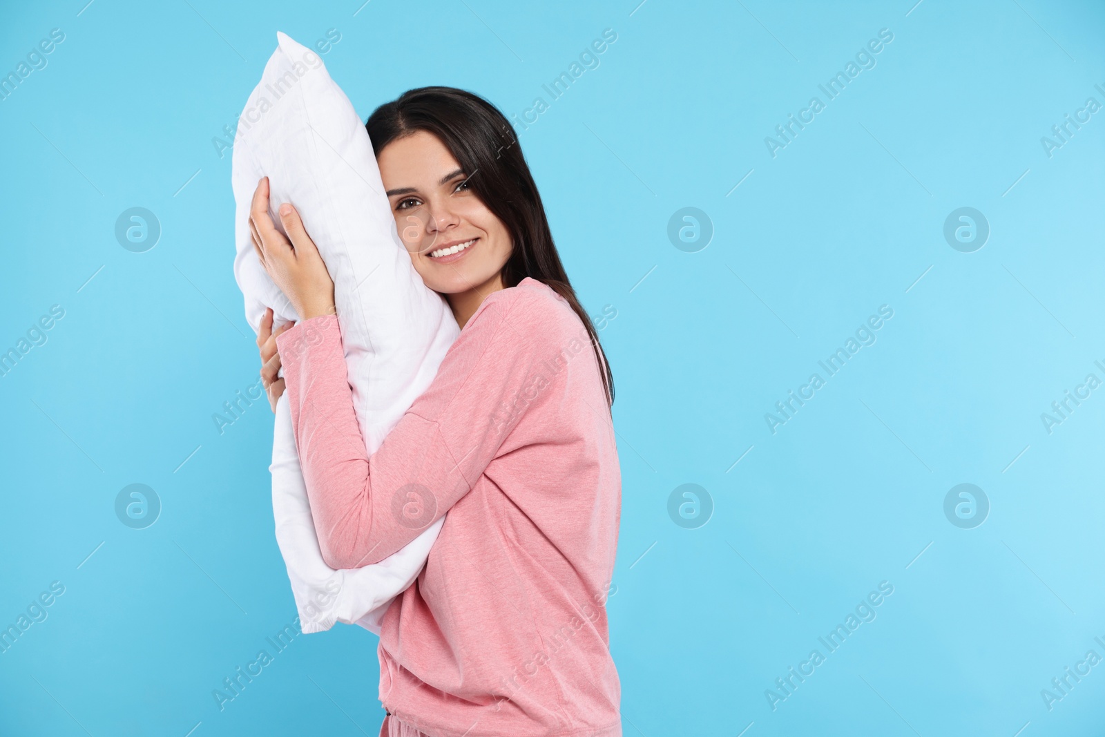 Photo of Happy young woman with soft pillow on light blue background, space for text