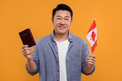 Photo of Immigration. Happy man with passport and flag of Canada on orange background