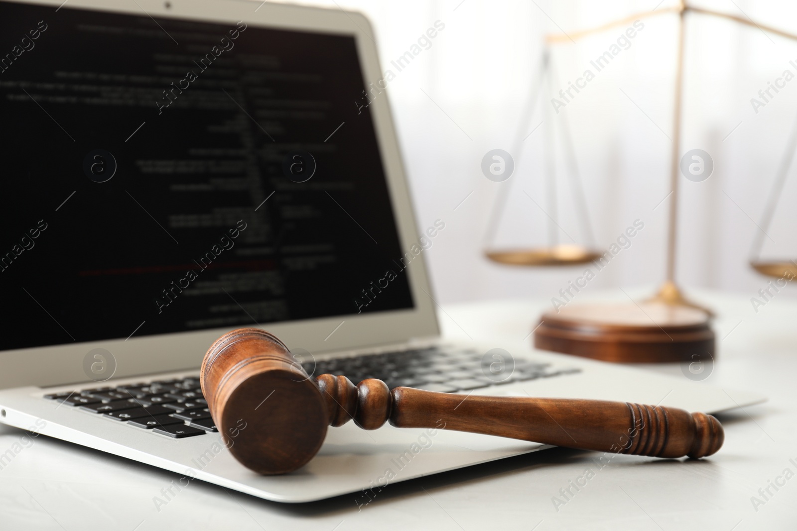 Photo of Laptop, wooden gavel and scales on white table, closeup. Cyber crime