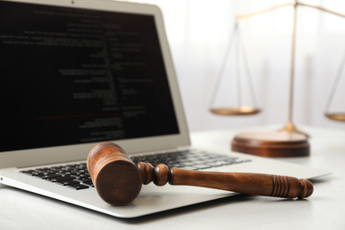 Laptop, wooden gavel and scales on white table, closeup. Cyber crime