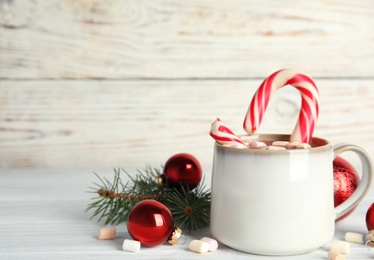 Photo of Cup of tasty cocoa with marshmallows, candy cane and Christmas decor on white wooden table. Space for text