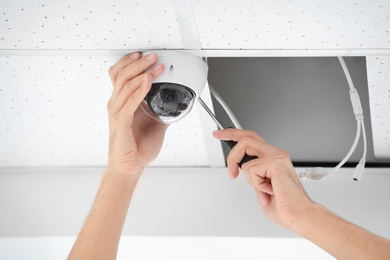 Photo of Technician installing CCTV camera on ceiling indoors, closeup