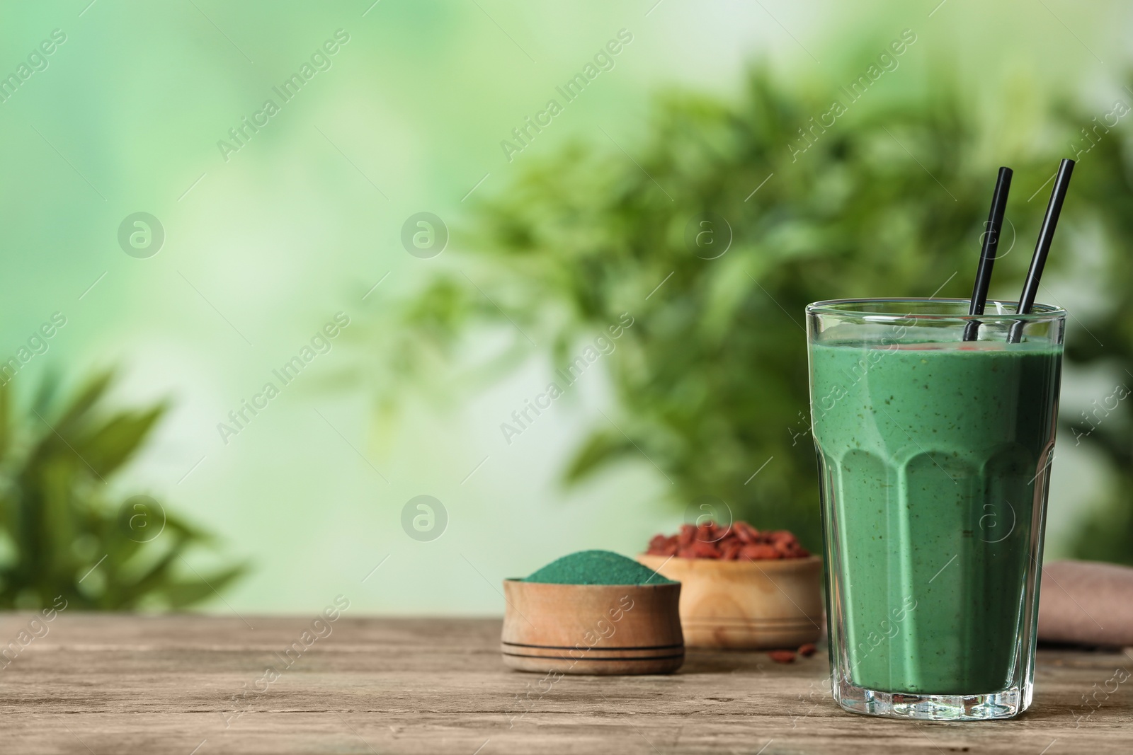 Photo of Glass of spirulina smoothie on table against blurred background. Space for text