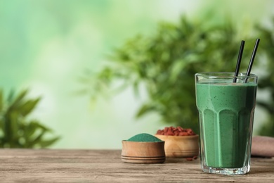 Photo of Glass of spirulina smoothie on table against blurred background. Space for text