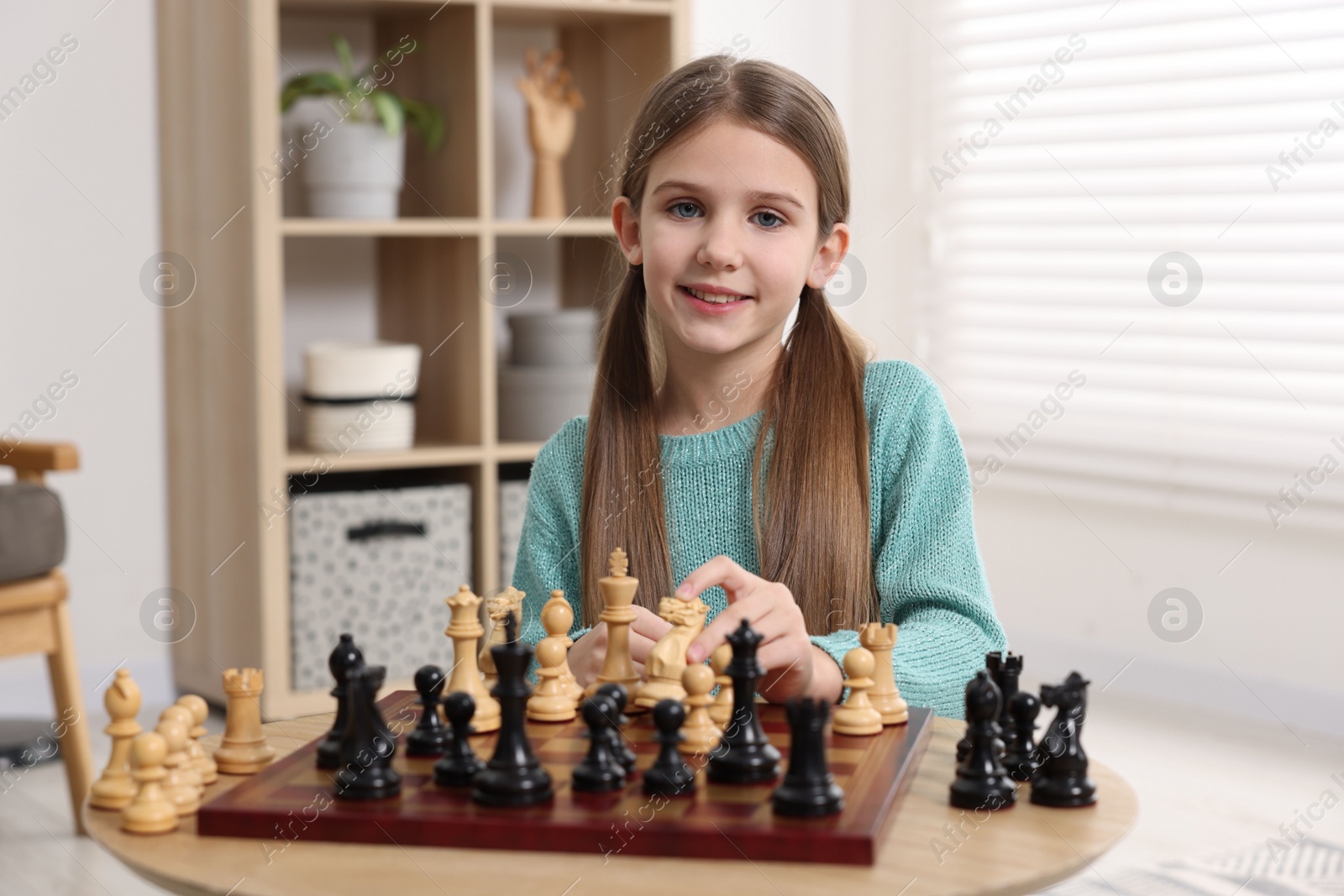 Photo of Cute girl playing chess at table in room