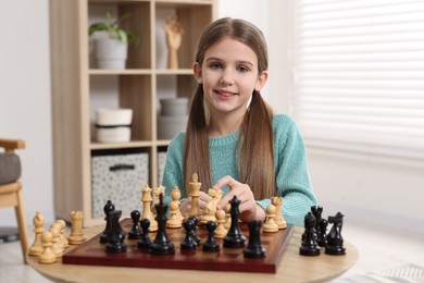 Photo of Cute girl playing chess at table in room