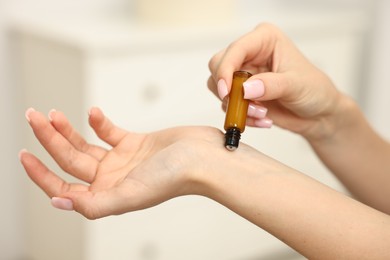 Photo of Aromatherapy. Woman with roller bottle applying essential oil onto wrist against light background, closeup