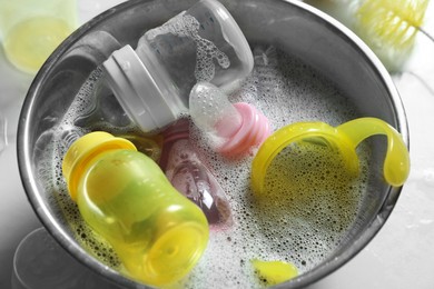 Metal bowl with baby bottles on white table, above view