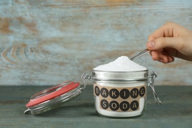 Photo of Woman taking baking soda with spoon from jar at light blue wooden table, closeup