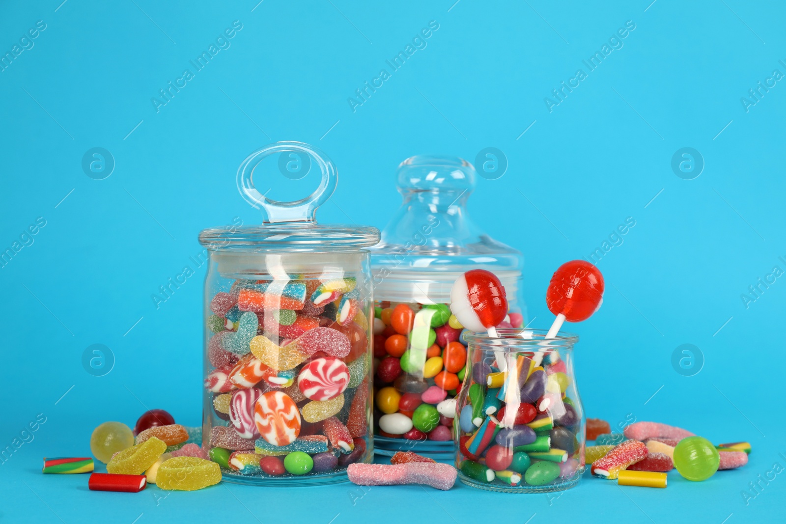 Photo of Glass jars with lots of different candies on light blue background