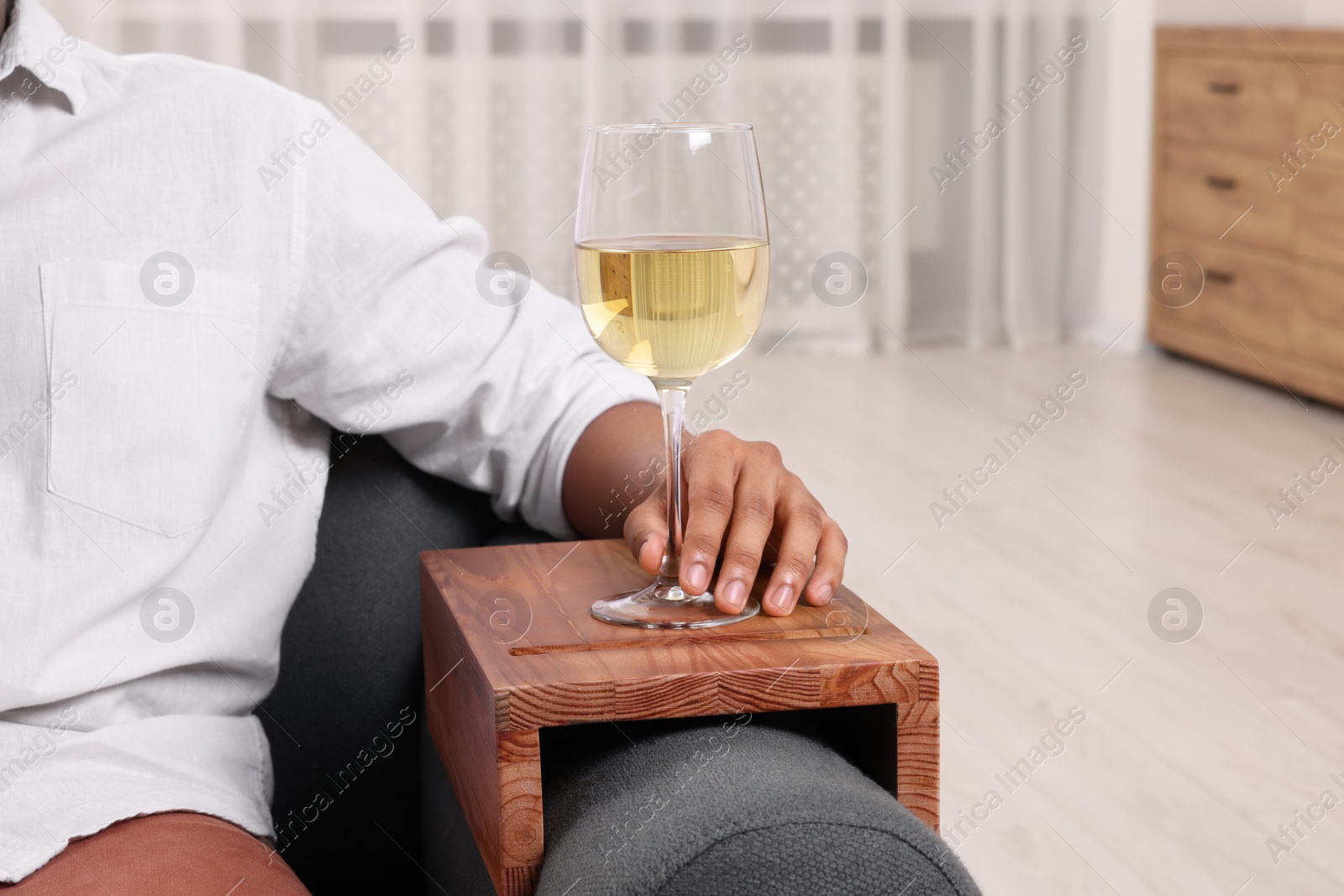 Photo of Man holding glass of wine on sofa armrest wooden table at home, closeup. Space for text