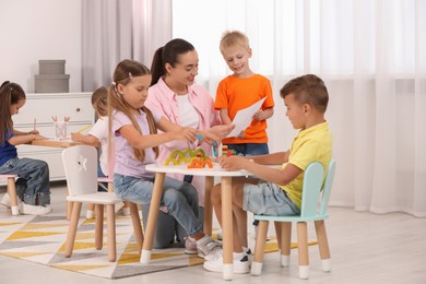 Photo of Nursery teacher and group of cute little children playing at desks in kindergarten. Activities for motor skills development